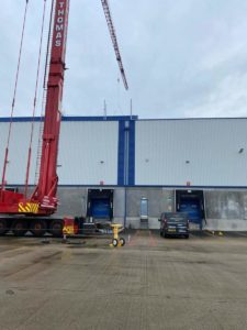 Photo Of Crane Lifting Metal Structure Onto Warehouse